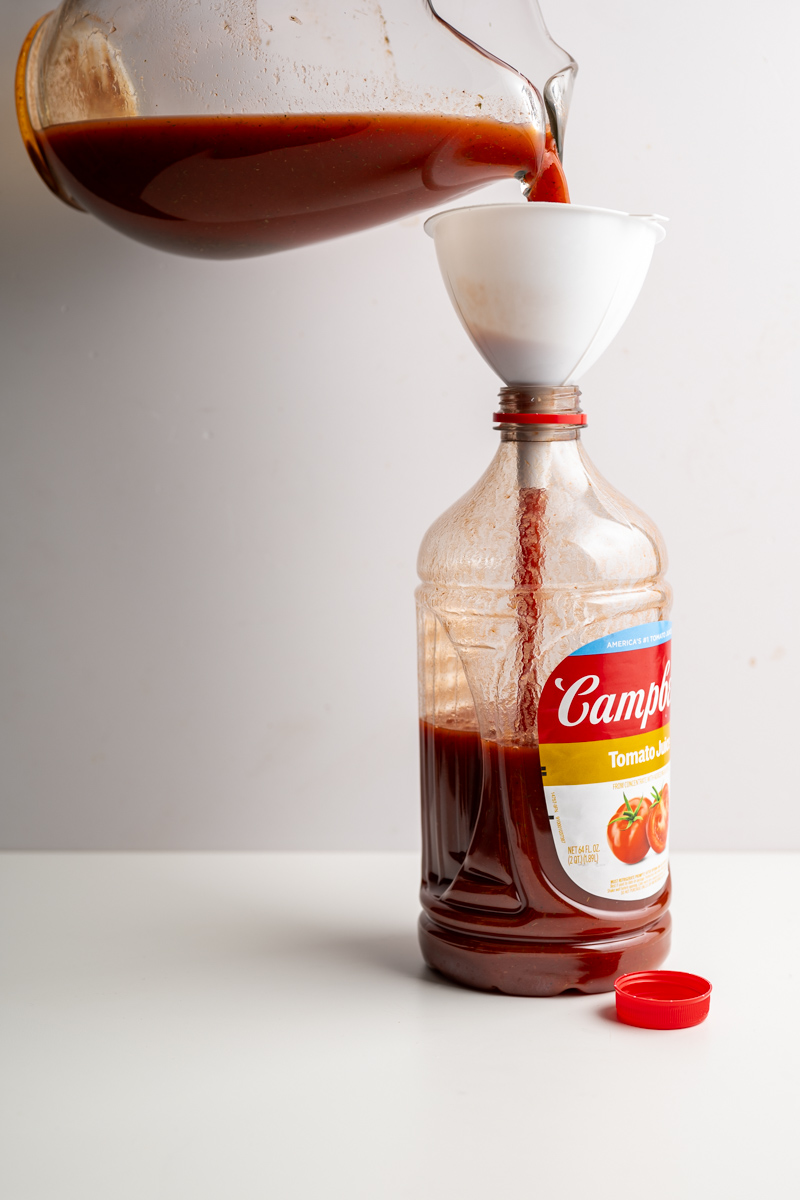 a glass pitcher pouring into a empty jug of tomato juice.