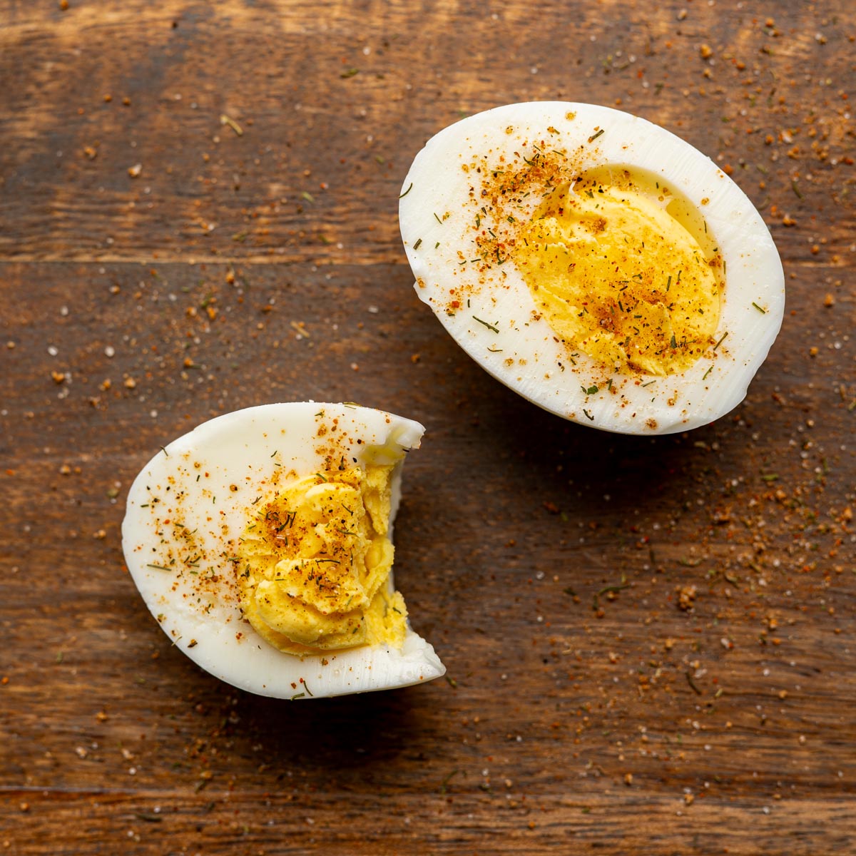 half of a hard boiled egg sprinkled with bloody mary seasoning on a wooden board.