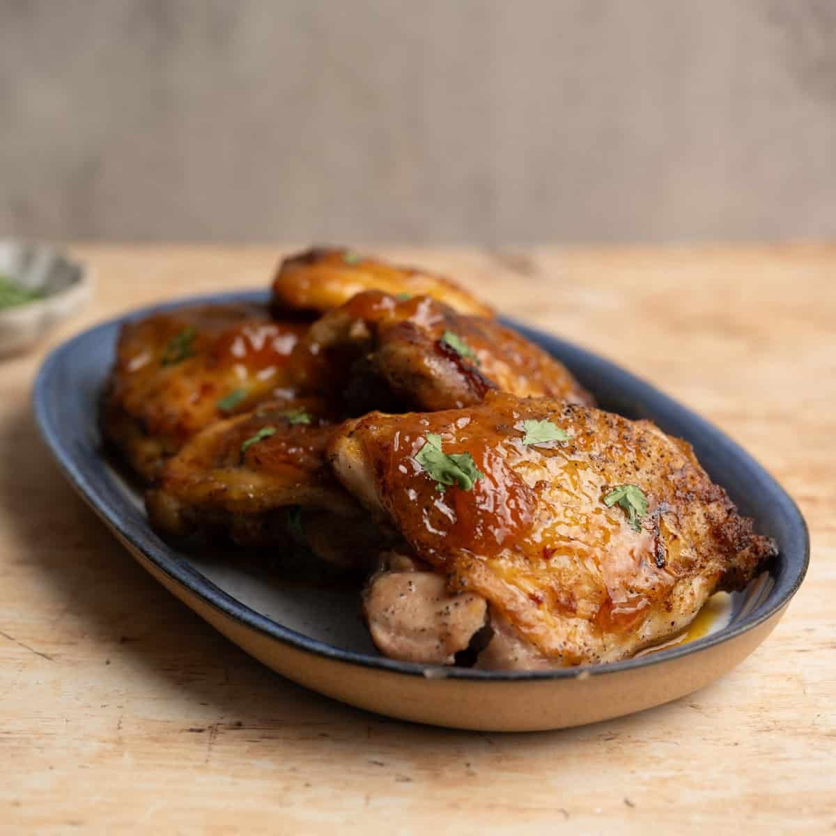 cooked chicken thighs on a blue platter on a wooden table.