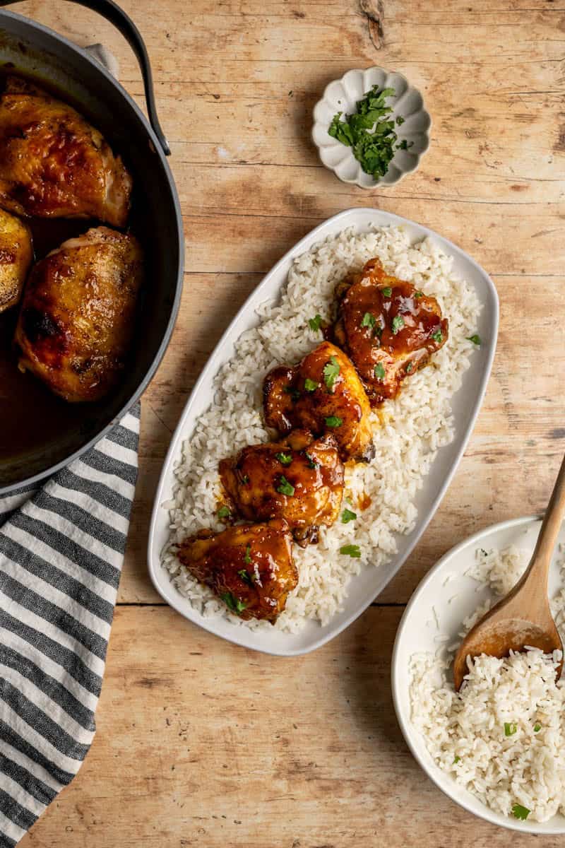 white platter with apricot curry chicken on a bed of rice along with side dish of rice and a skillet with more chicken thighs.