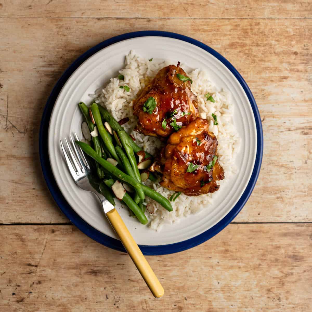 plate with two apricot curry chicken thighs on a bed of rice with green beans.