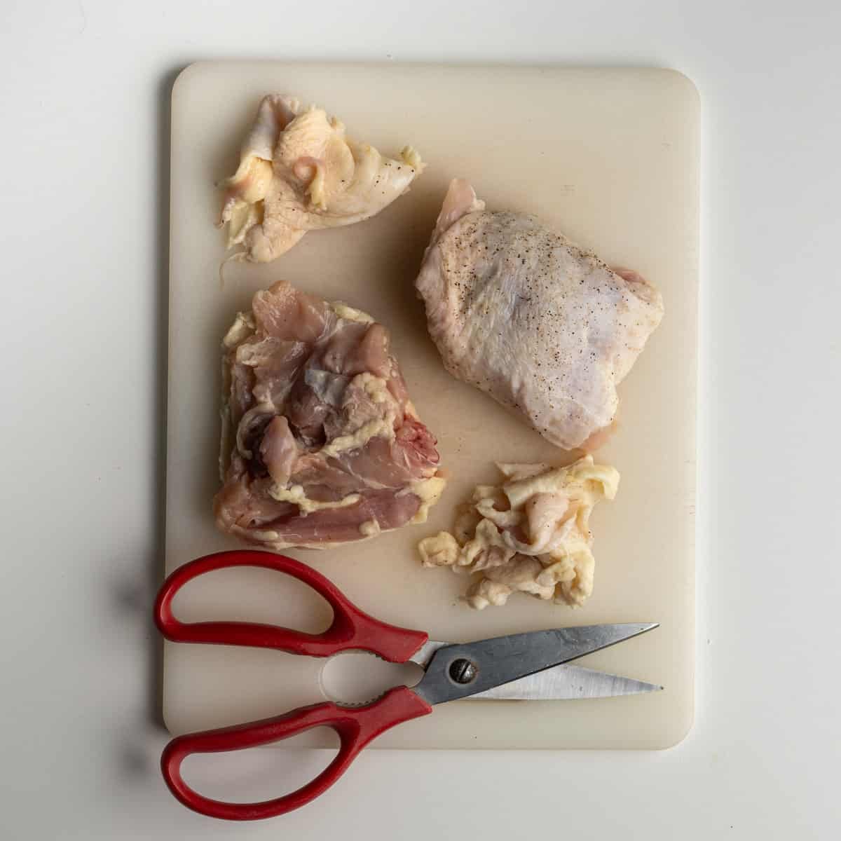 cutting board with two chicken thighs alongside a kitchen shears.