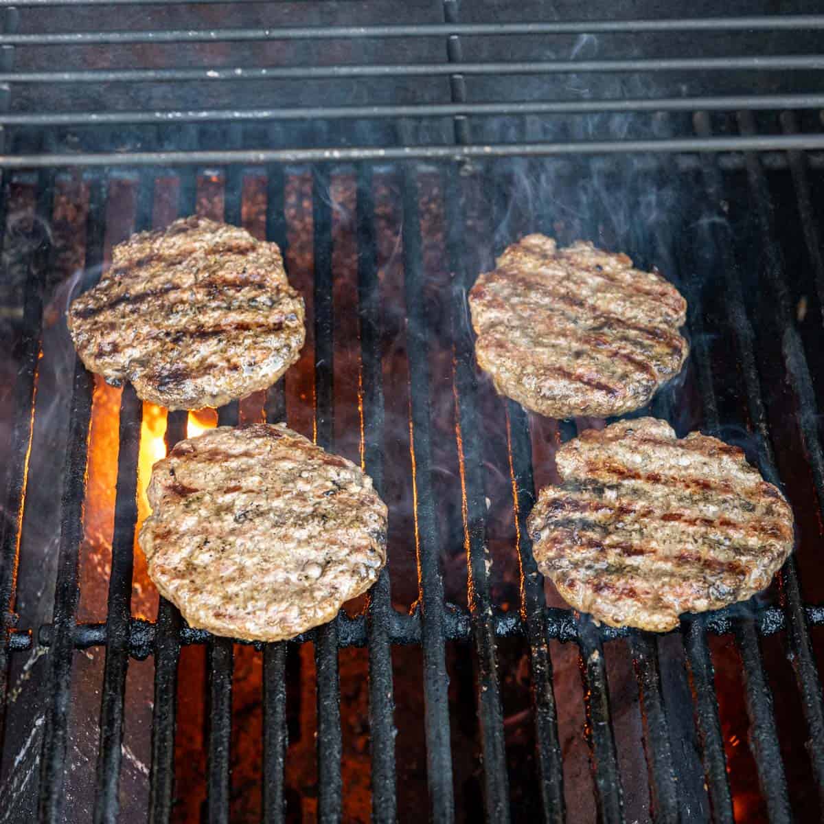 four burgers on a grill with grill marks.