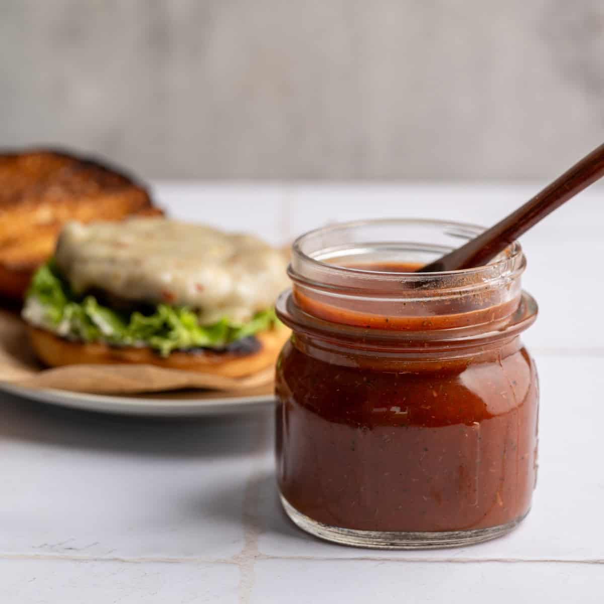 small jar of bloody mary ketchup in front of an open face burger being built on a plate.