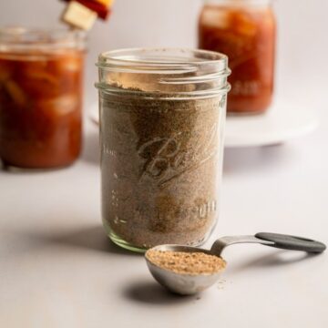 mason jar filled with bloody mary seasoning with two bloody mary drinks in the background.