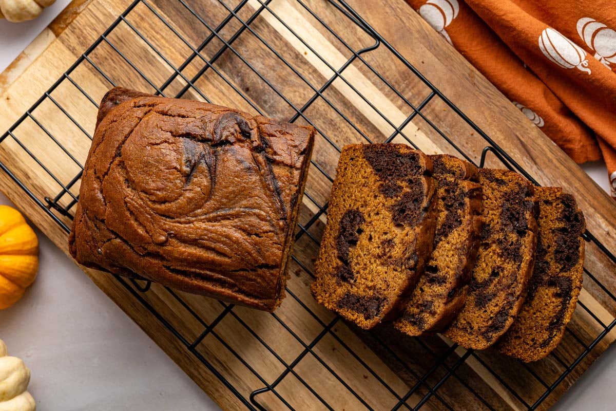 sliced pumpkin chocolate swirl bread on a cooling rack and cutting board.