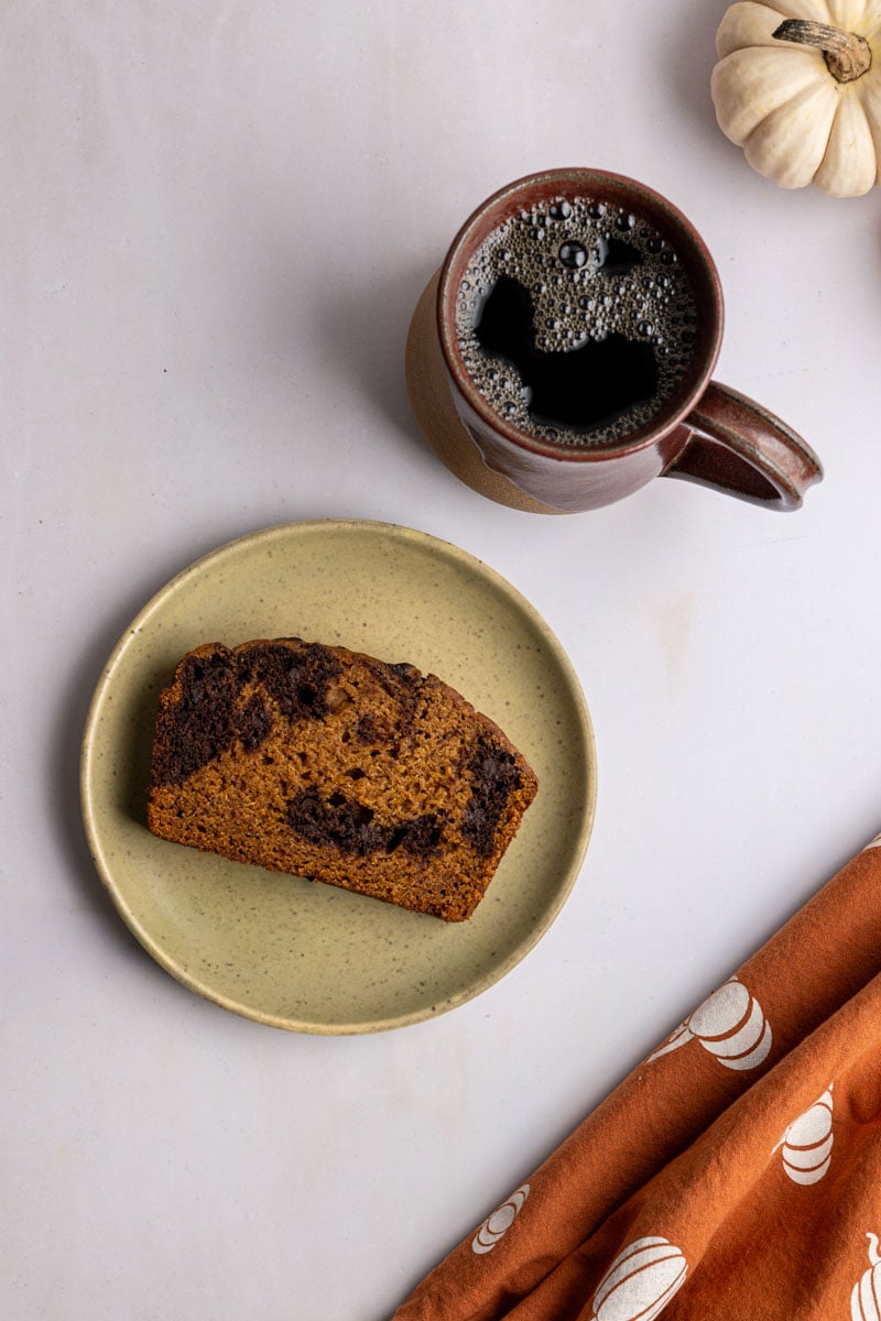 slice of pumpkin bread on a plate with a cup of coffee.