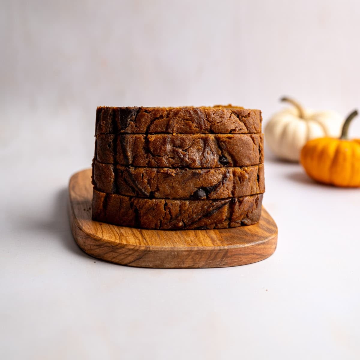 sliced pumpkin bread stacked on a wooden cutting board.