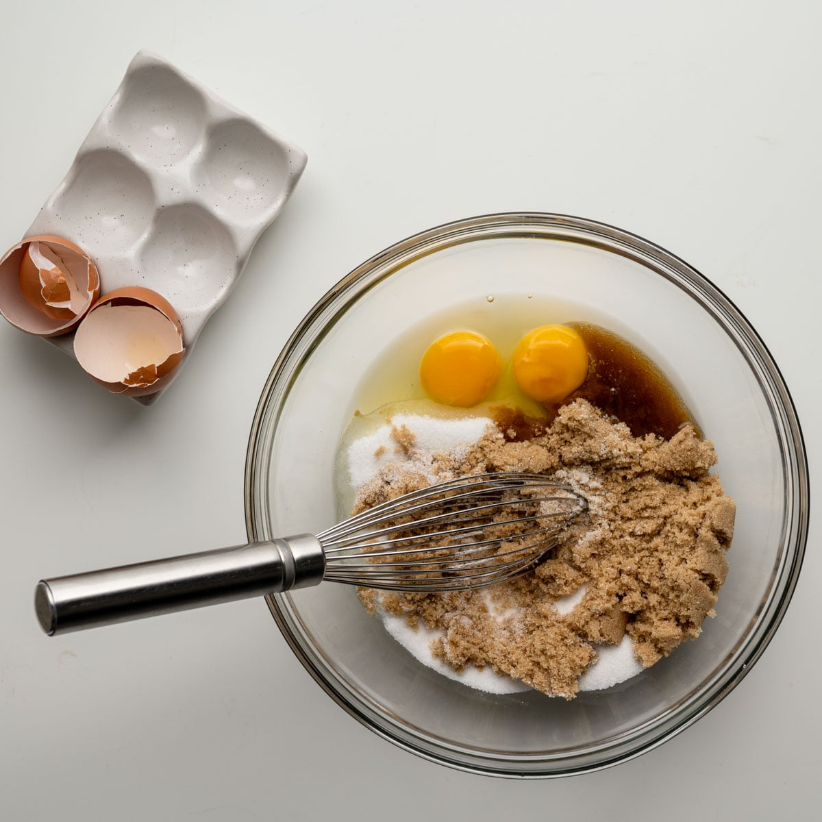 eggs, sugars in a glass bowl with a whisk.