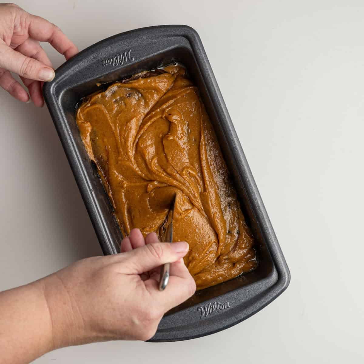 one hand holding a knife swirling the bread batter into a figure eight pattern.