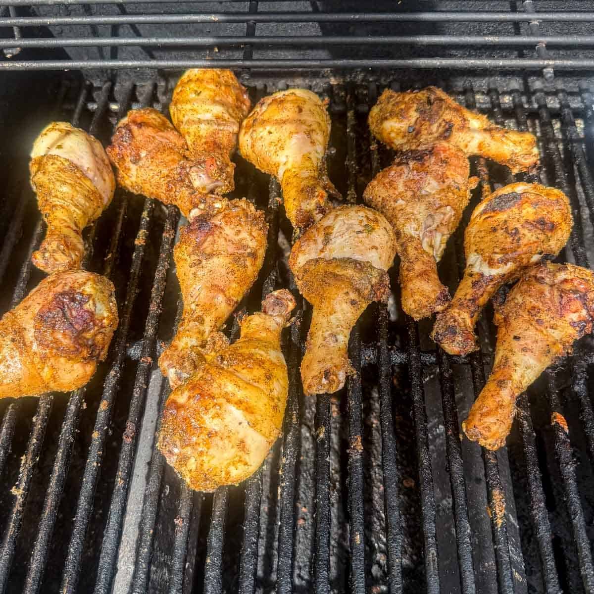 chicken drumsticks cooking on grill grates.
