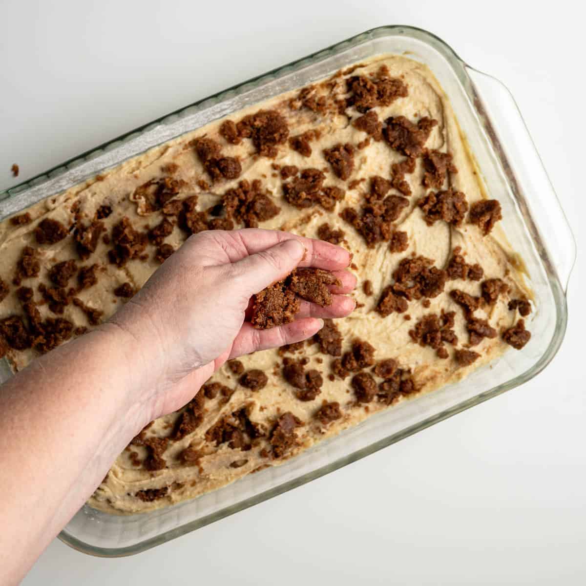 hand sprinkling streusel over the top of the coffee cake.
