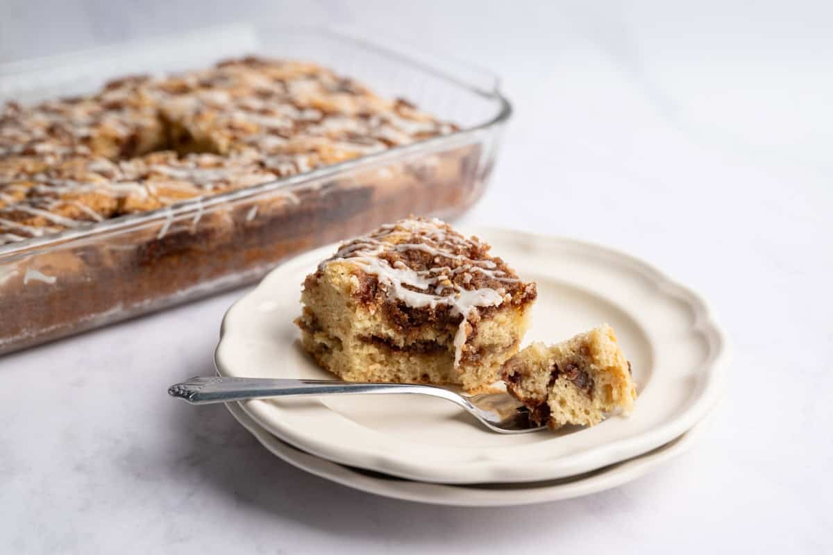 piece of cinnamon coffee cake with a bite missing on a fork with a pan of coffee cake in the background.