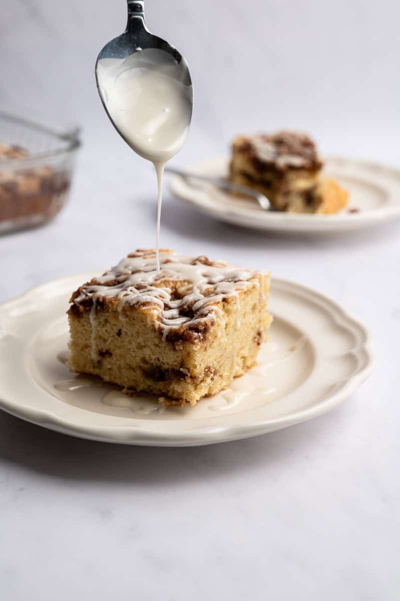 spoon drizzling glaze on an individual piece of cinnamon coffee cake.