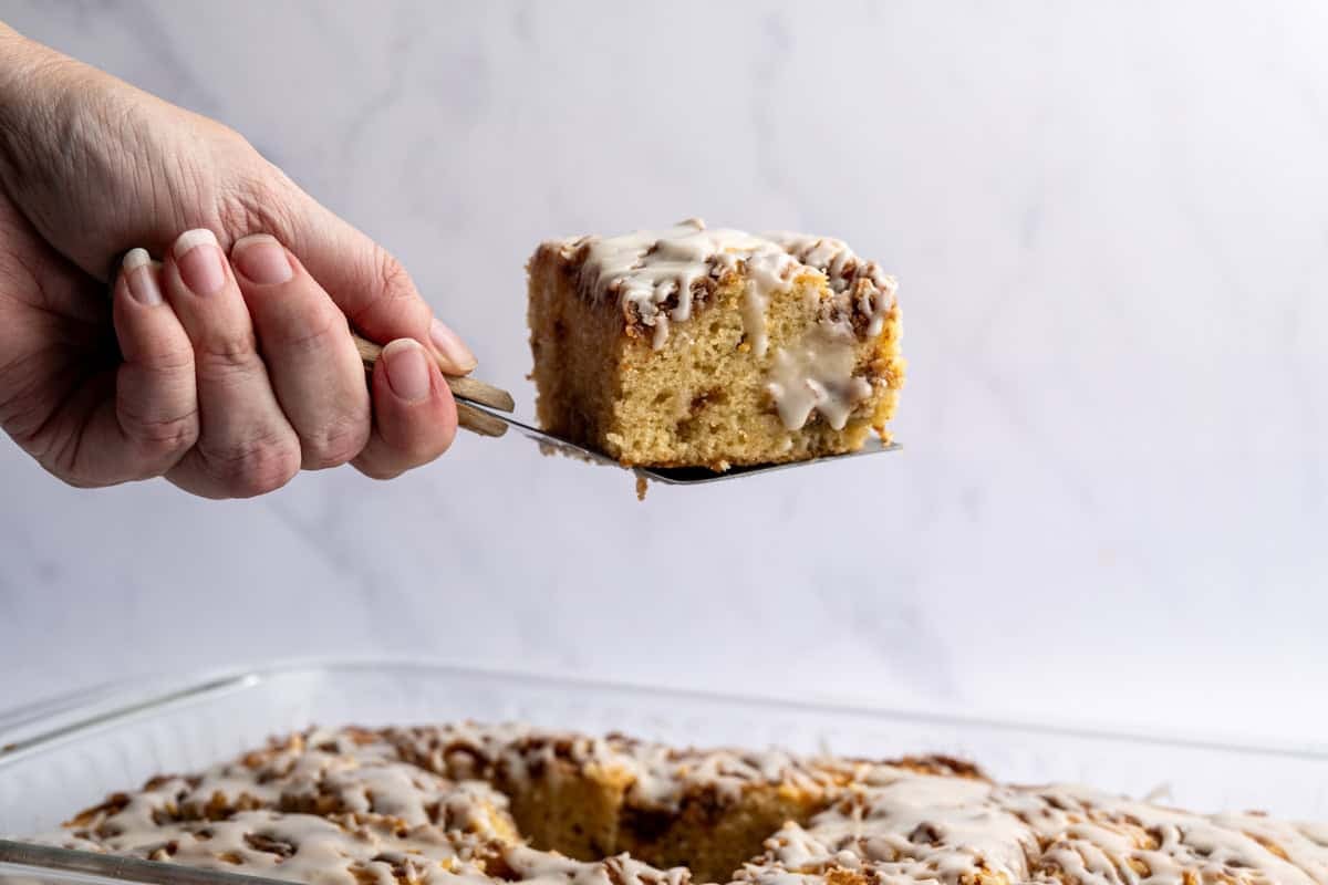 a single piece of cinnamon coffee cake behing held above a pan of coffee cake.
