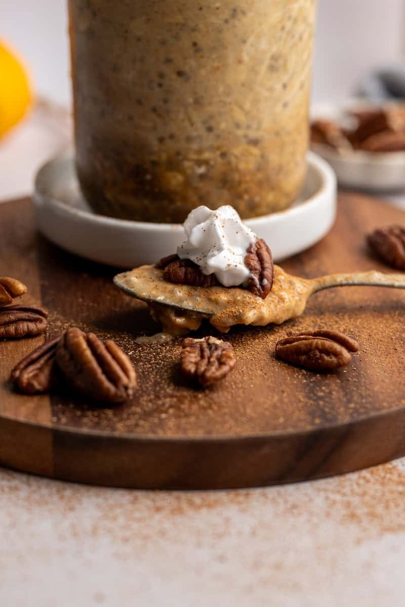 spoonful of pumpkin overnight oats topped with coconut whipped cream, a pecan and cinnamon.