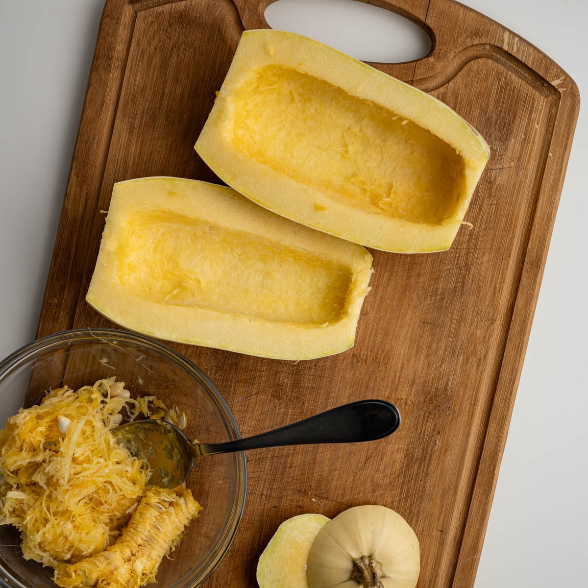 spaghetti squash halved, scraped of the seeds on a wooden cutting board.