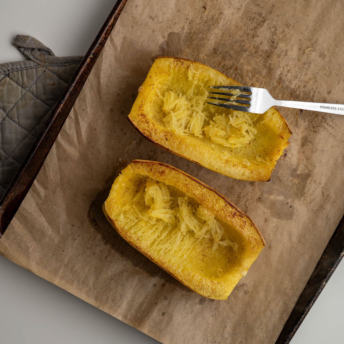 baked spaghetti squash with a fork pulling strands inside the squash.
