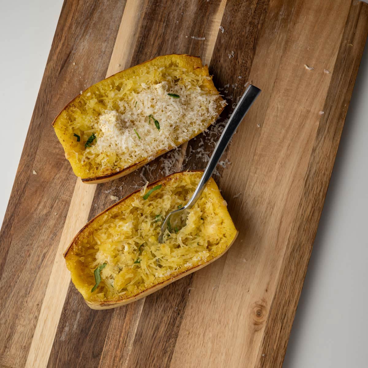 fork pulling out a bite of spaghetti squash on a wooden board.