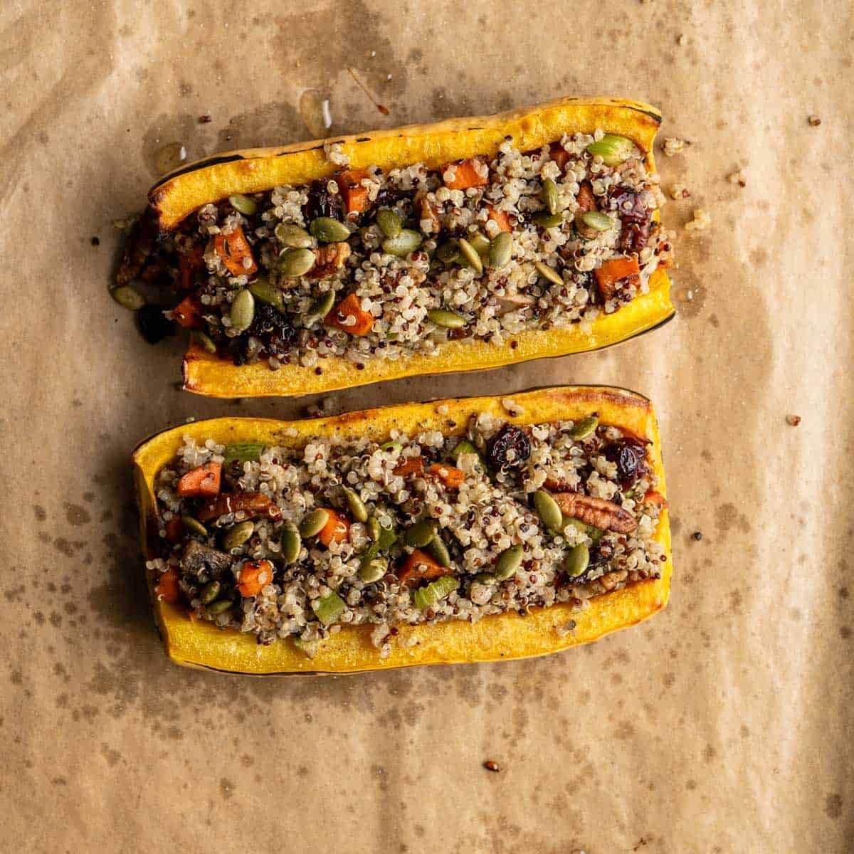 stuffed delicata squash halves with qunioa stuffing mix on a baking sheet.