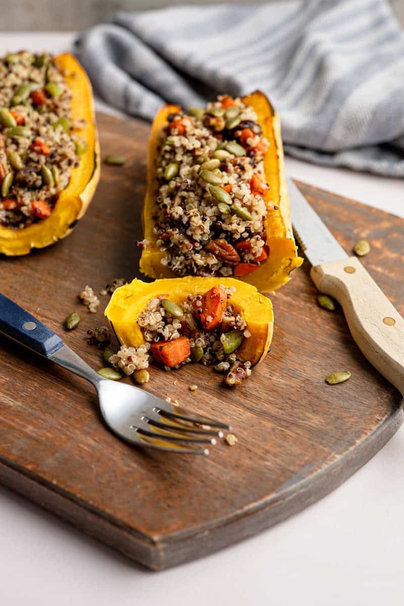 stuffed delicata squash with a slice cut off on a wooden board with a fork and knife.