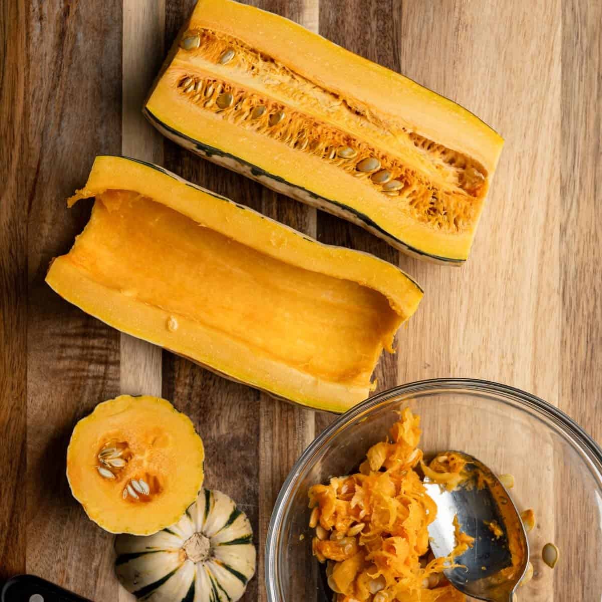 sliced delicata squash on a wooden board with one half seeds removed in a glass bowl.