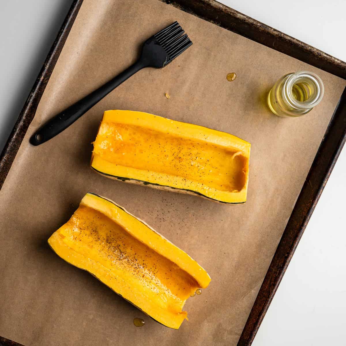 delicata squash halves brushed with garlic infused olive oil on a baking sheet covered with parchment paper.