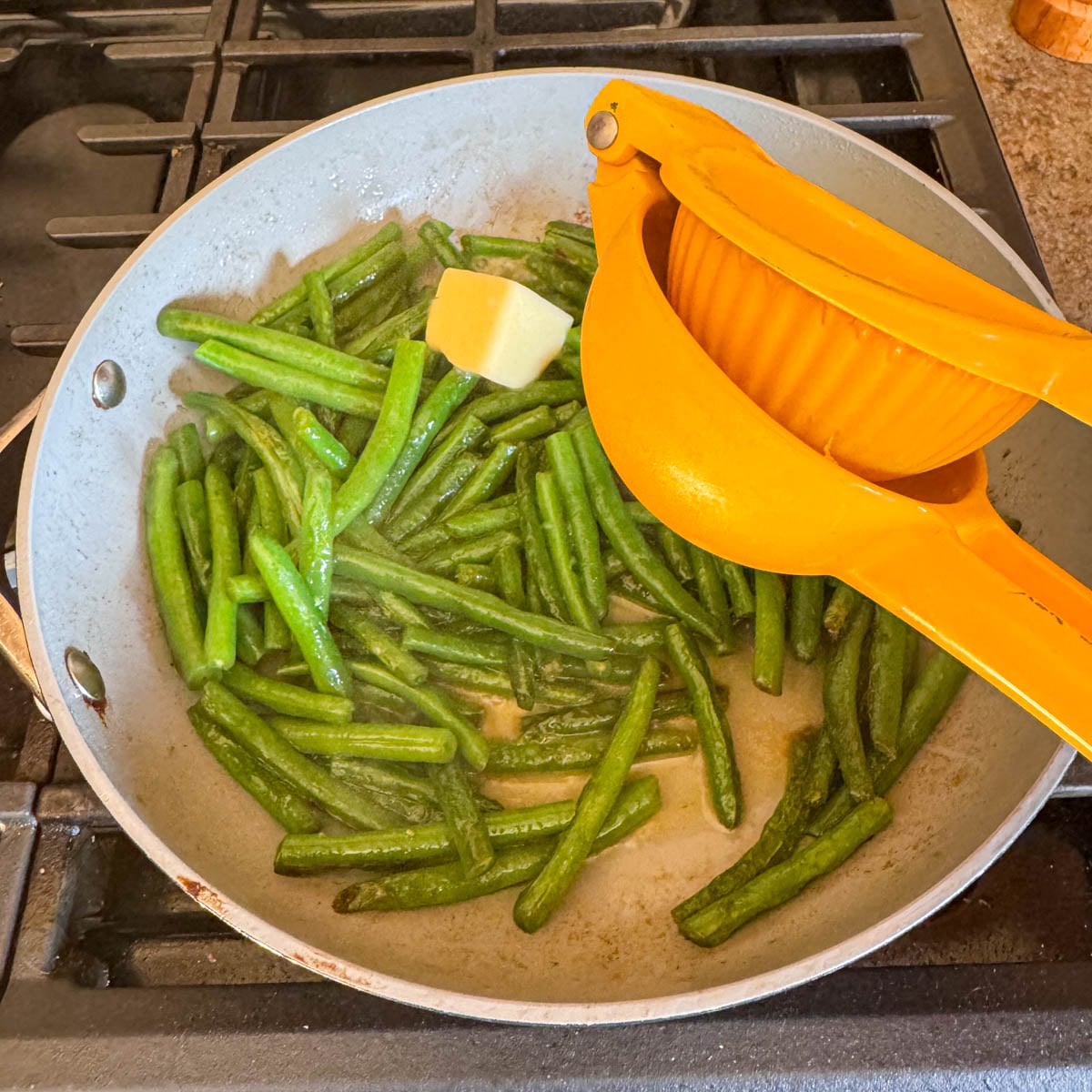 cooked green beans with a butter, and a citrus juicer with a fresh lemon in a skillet.