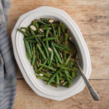cooked fresh green beans in a white serving dish with a serving spoon.