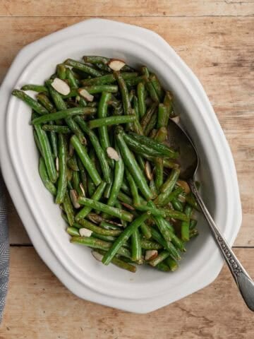 cooked fresh green beans in a white serving dish with a serving spoon.