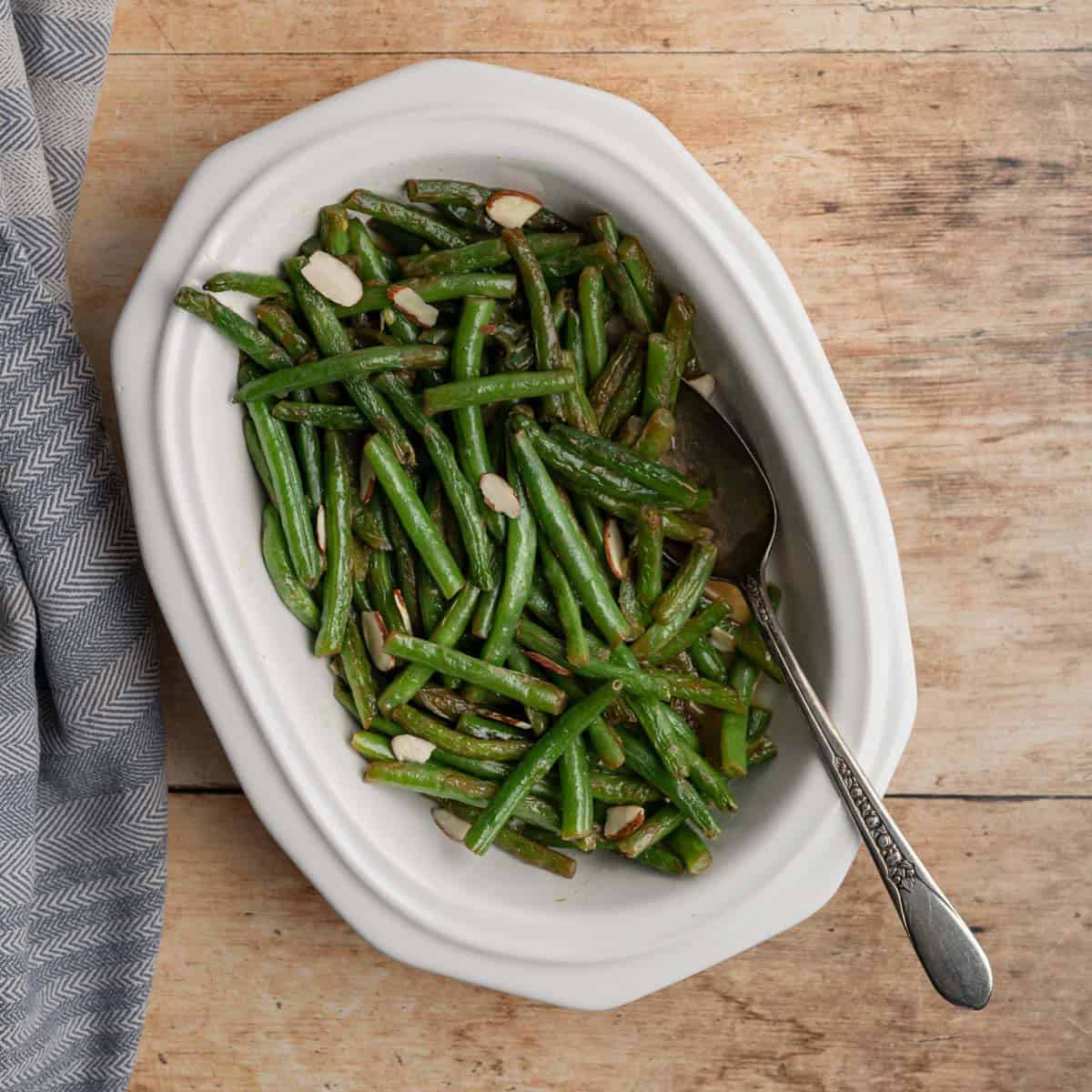 cooked fresh green beans in a white serving dish with a serving spoon.