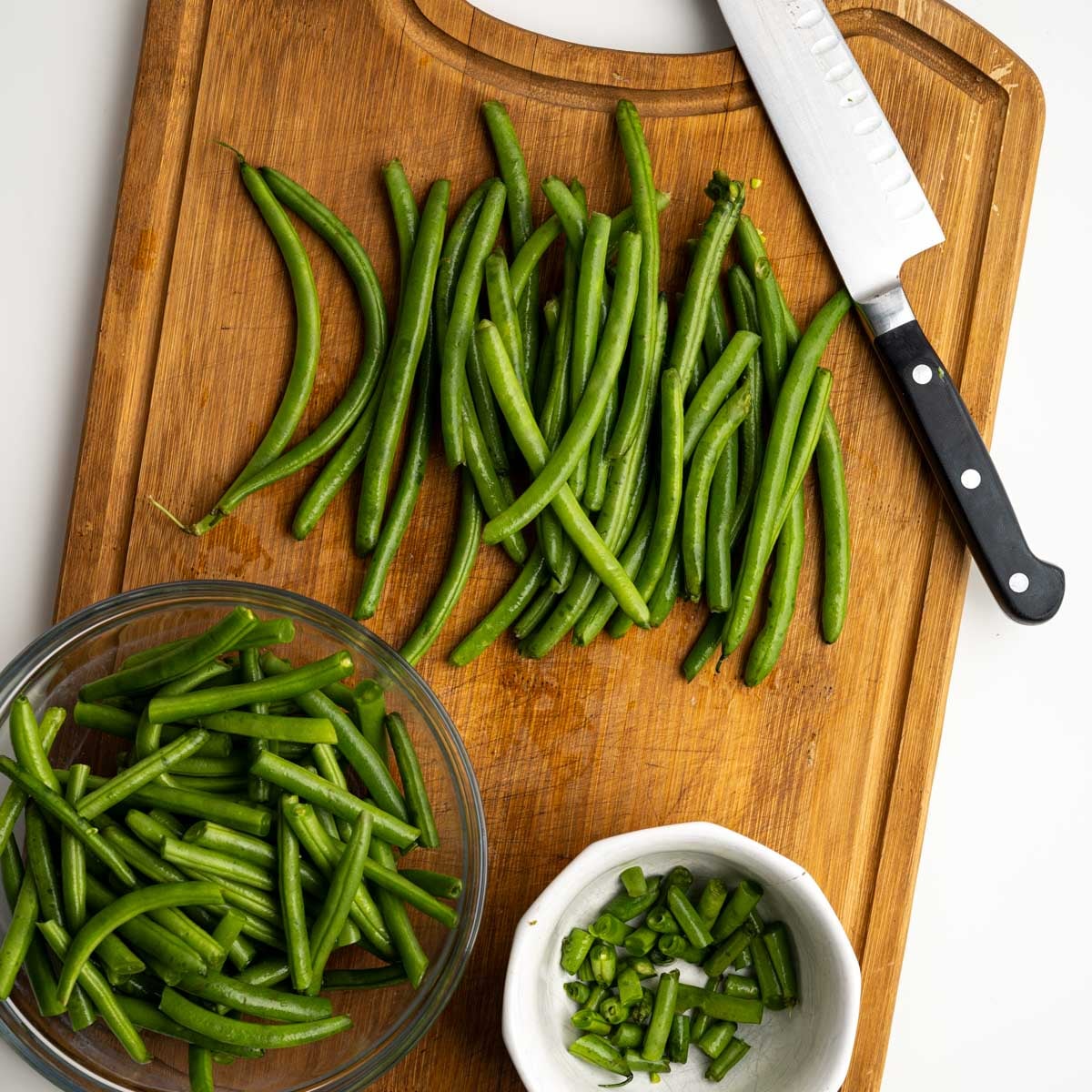 fresh green beans on a wooden cutting board with knife.