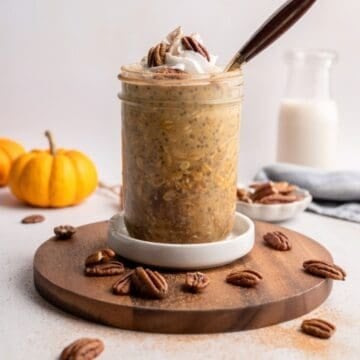 jar of pumpkin overnight oats topped with coconut whipped cream dusted with cinnamon and pecans.