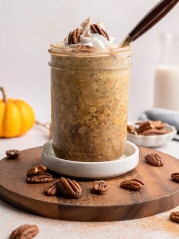 jar of pumpkin overnight oats topped with coconut whipped cream dusted with cinnamon and pecans.