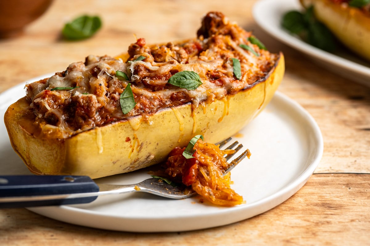spaghetti squash boat stuffed with Italian turkey sausage, tomatoes and topped with cheese on a white plate.