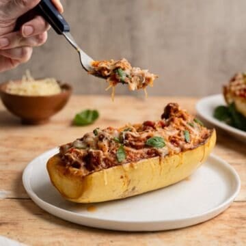 hand holding a forkful of stuffed spaghetti squash above a spaghetti squash boat.