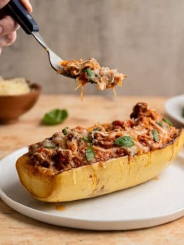 hand holding a forkful of stuffed spaghetti squash above a spaghetti squash boat.