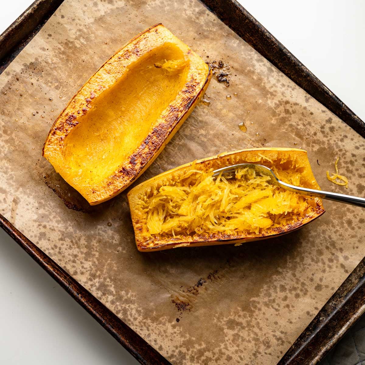 roasted spaghetii squash on a baking sheet with a fork pulling the strands of squash.