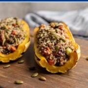 two delicata squash halves stuffed with quinoa , veggies, pecans and cranberries stuffed inside on a wooden board.